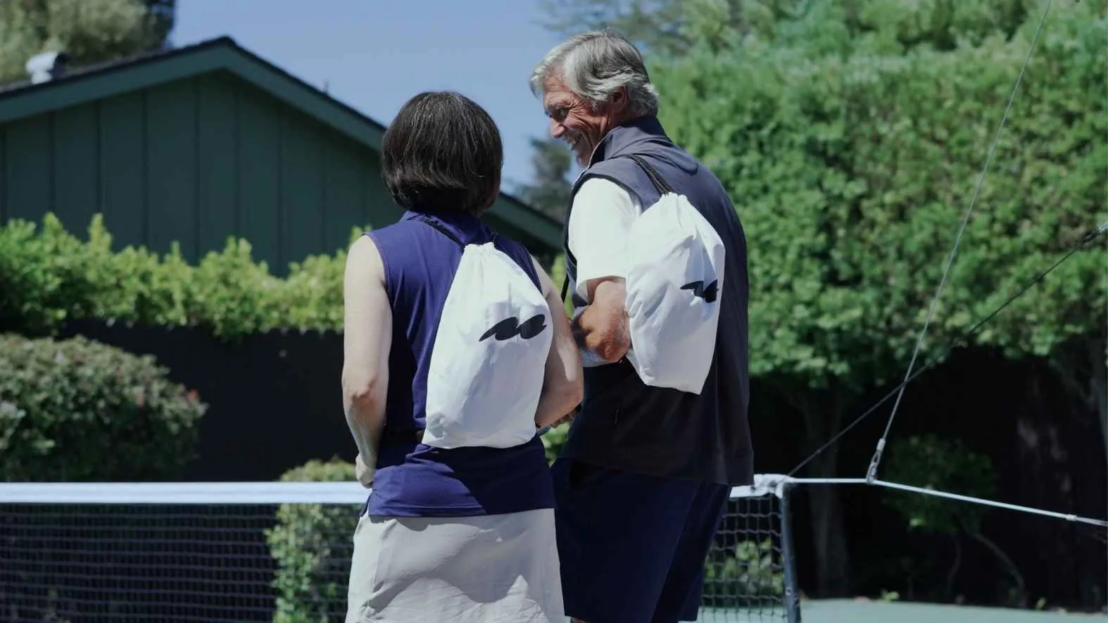 Two players on a tennis court carrying CUURT bags